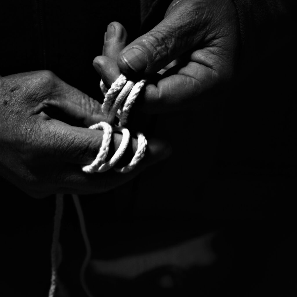 Close-up black-and-white photo of two pairs of hands tying rope together