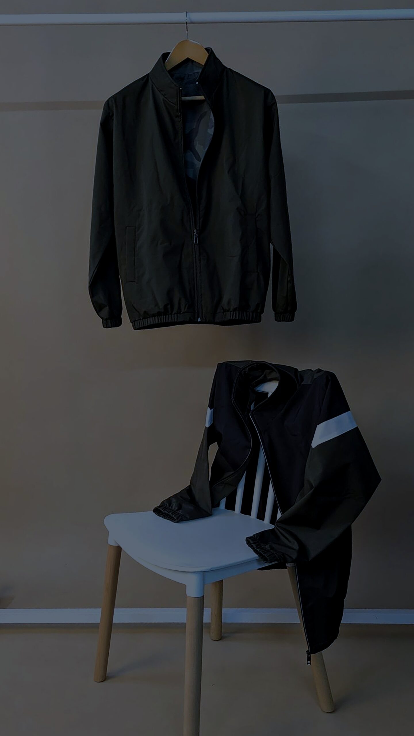 A black jacket hanging on a wall next to a white chair