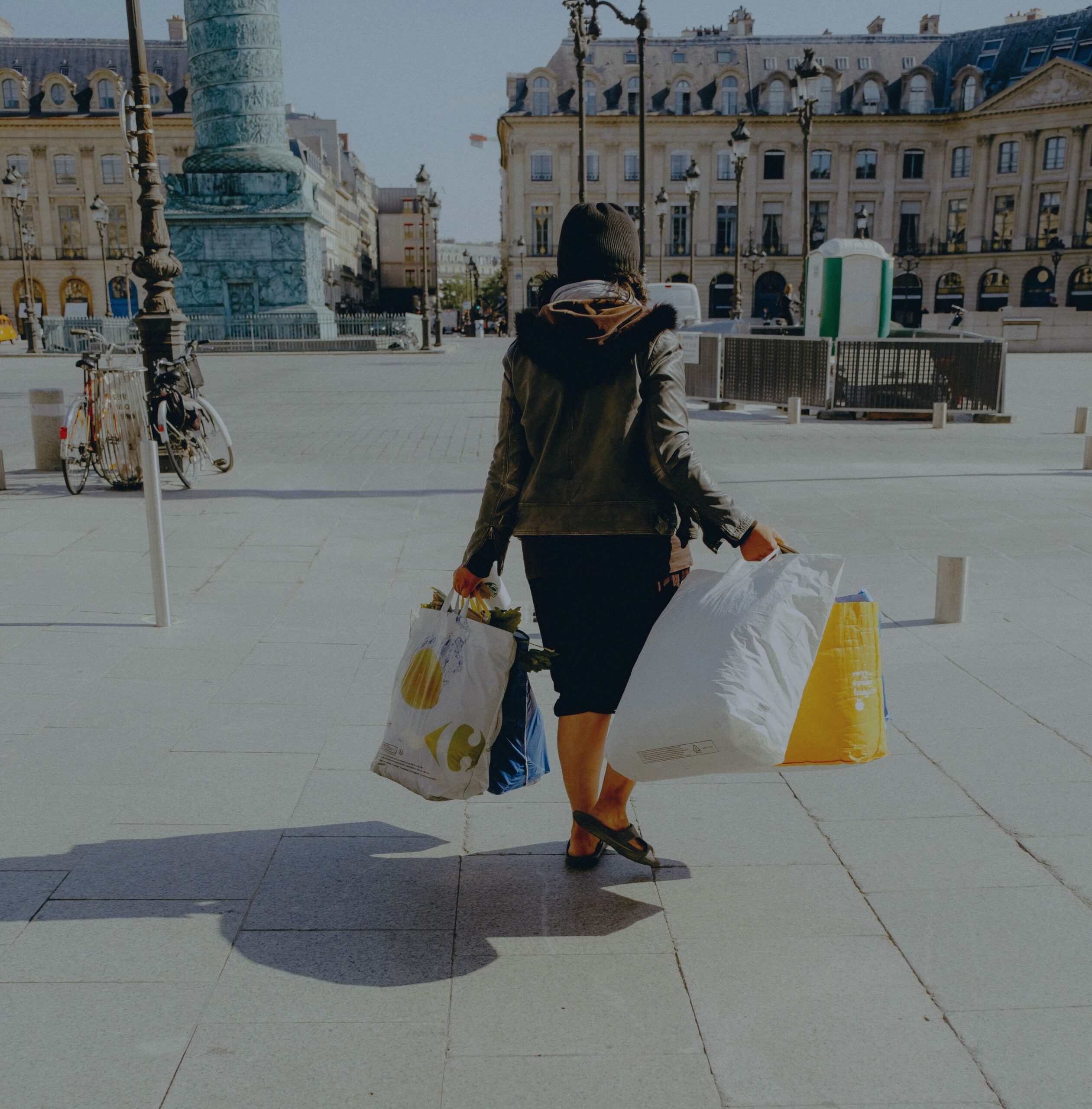 Woman from behind, carrying multiple shopping bags in a European plaza