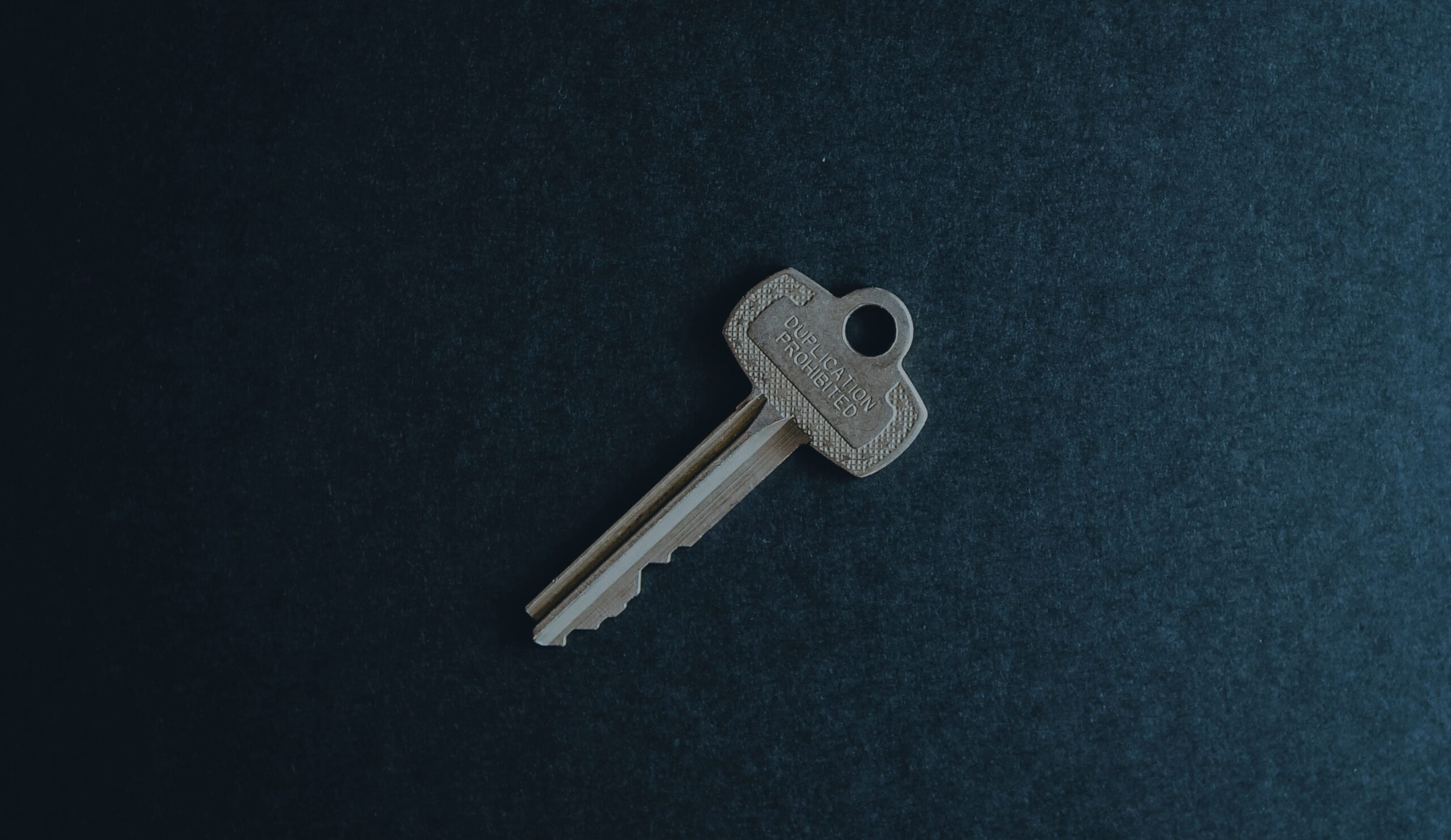 A single office key resting on a dark surface, engraved "duplication prohibited"