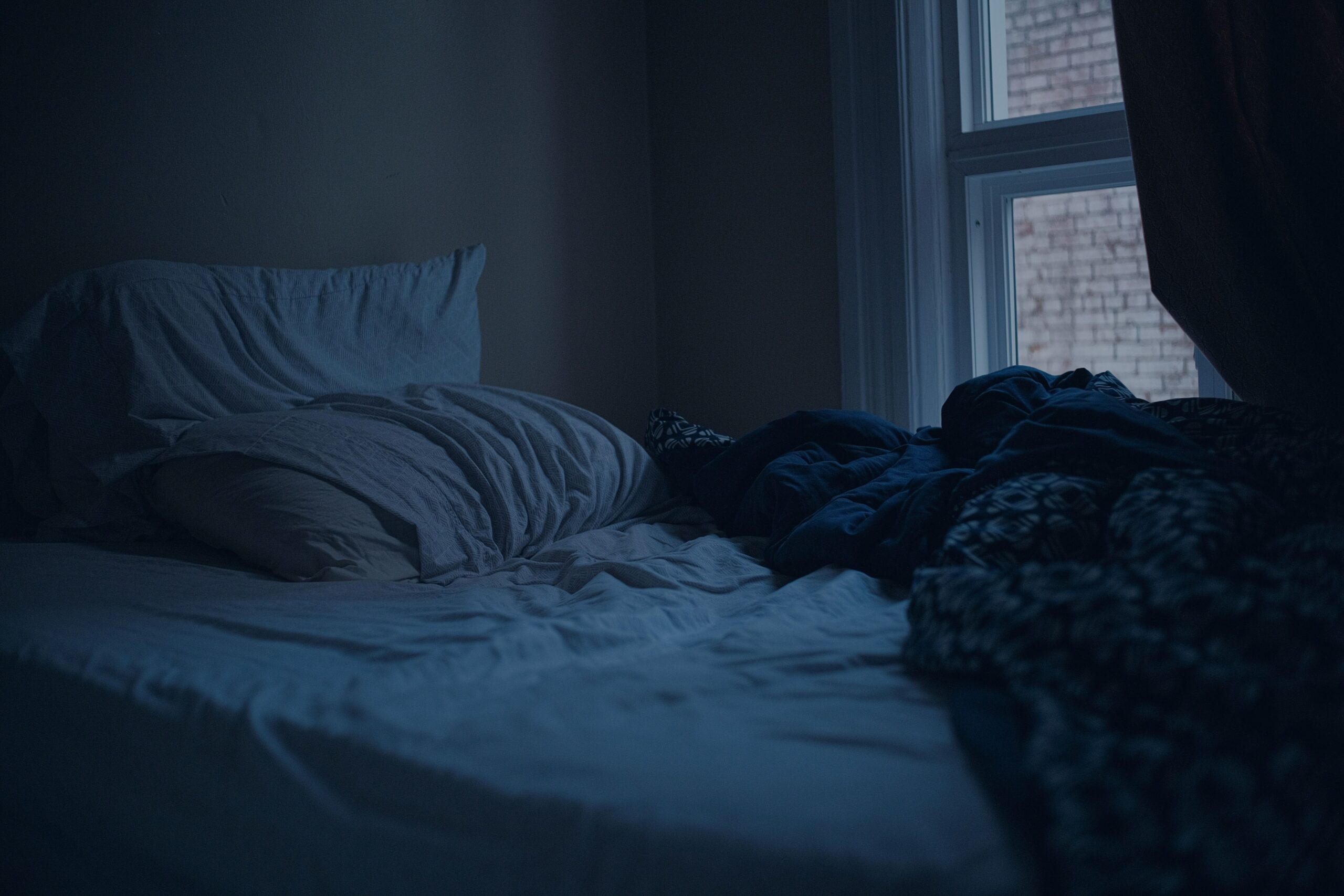 An unmade bed in a dark, quiet bedroom